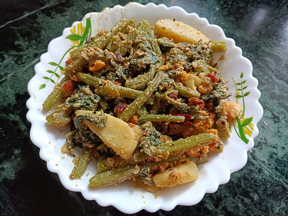 Un bol blanc contenant du « Laau shaaker posto », un plat typiquement bengali à base de tiges et de feuilles de courge calebasse, de pommes de terre et de « bori », des boulettes de pâte de lentilles séchées au soleil. Le tout est cuit dans une pâte de graines de pavot et de moutarde.