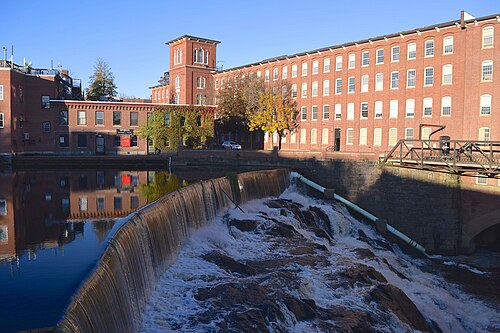 Un bâtiment en briques rouges construit au-dessus d'une cascade. La cascade est une structure de barrage en béton.