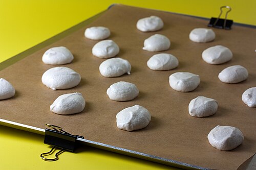 Une feuille de métal, recouverte de papier kraft. Le papier est fixé sur le côté du moule. Il y a des biscuits sur le papier, prêts à cuire.