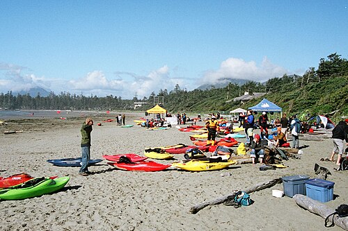 Photo d'une plage avec plusieurs kayaks éparpillés et des gens en arrière-plan