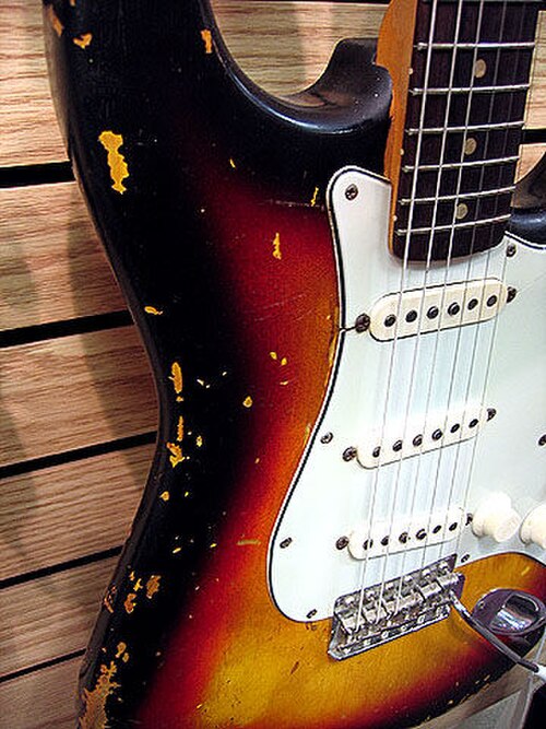 Stratocaster de 1963 avec corps en aulne, touche en palissandre, pickguard à trois plis et finition sunbirth tricolore. La laque nitrocellulosique présente des écaillures caractéristiques dues à l'utilisation.