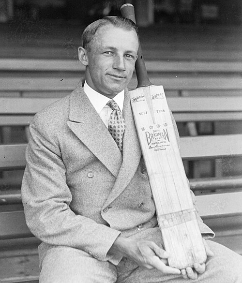 Homme en costume croisé, posant avec une batte de cricket.