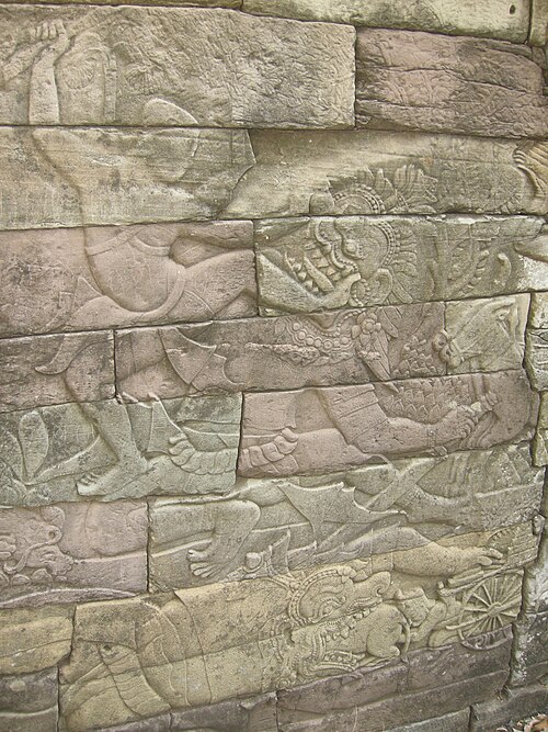 Un coup de pied porté à un ennemi abattu ou en train de tomber (un démon), bas-relief de la période d'Angkor (vers le XIIIe siècle) à Banteay Chhmar au Cambodge.
