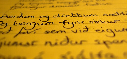Photo d'un texte manuscrit noir sur un papier apparemment jaune avec le haut et le bas flous et le milieu vertical clair