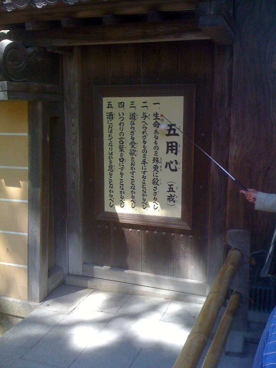 Plaque avec des caractères chinois écrits verticalement. Une main masculine pointe vers eux avec un pointeur.