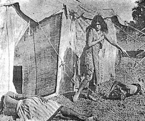 Une jeune femme aux longs cheveux noirs sort d'une tente, regardant l'un des deux hommes endormis sur le sol. Elle ne porte qu'un châle et une robe qui lui arrive aux genoux, laissant ses bras, ses jambes et ses pieds exposés.
