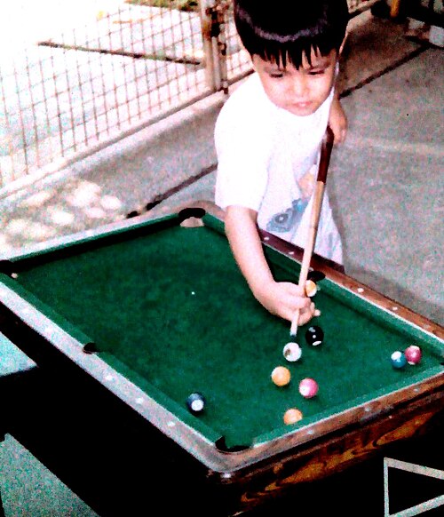 Un enfant joue à un billard miniature posé sur une table basse et utilisant de petites boules.