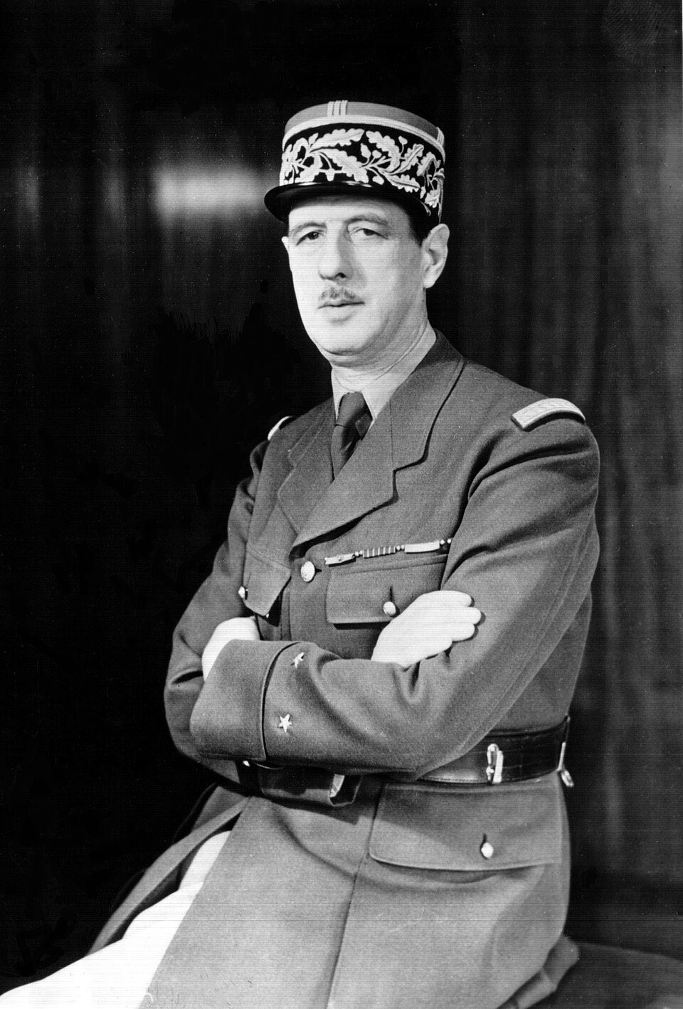 Charles de Gaulle assis en uniforme, regardant vers la gauche, les bras croisés