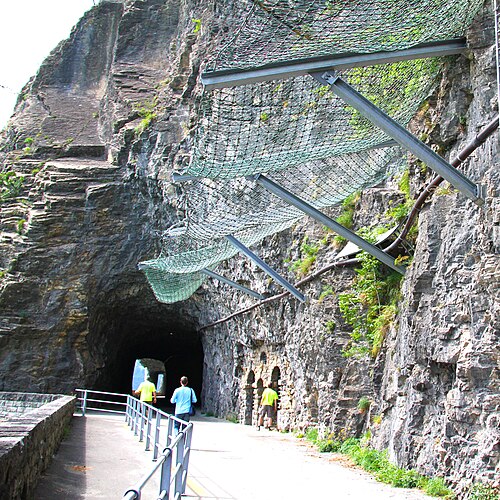 Image d'un tunnel rocheux (arrière-plan) et d'un maillage de protection contre les chutes de pierres sur une paroi rocheuse (premier plan)