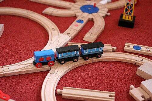 Petits trains bleus sur des rails en bois emboîtables sur un tapis rouge
