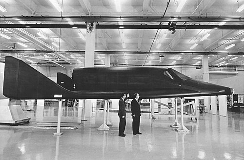 Des hommes se tiennent à côté d'un élégant avion spatial noir.