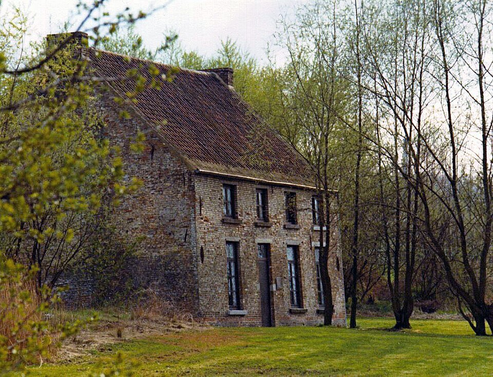 Photo d'une maison en briques de deux étages à gauche, partiellement masquée par des arbres, avec une pelouse à l'avant et une rangée d'arbres à droite.