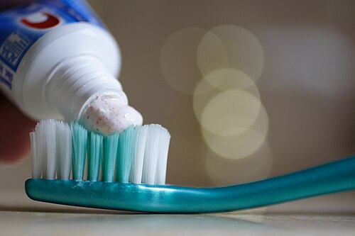 Photographie avec du dentifrice provenant d'un tube de dentifrice appliqué sur les poils d'une brosse à dents au premier plan
