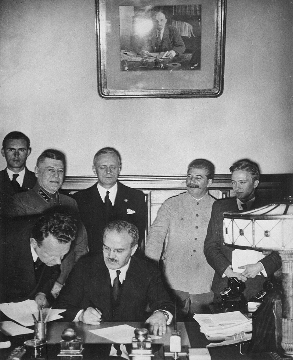 Le ministre soviétique des Affaires étrangères, Viatcheslav Molotov, signe le pacte Molotov-Ribbentrop. Derrière lui se tiennent le ministre allemand des Affaires étrangères, Joachim von Ribbentrop, et le Premier ministre soviétique, Joseph Staline.