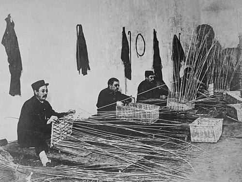 Photographie en noir et blanc de trois hommes tissant des paniers en osier