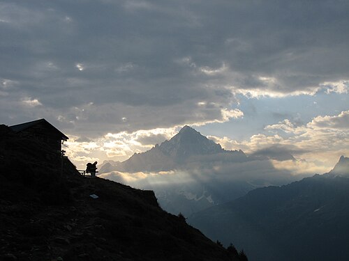 Un promeneur se dessine en silhouette près d'une cabane sur le versant d'une montagne