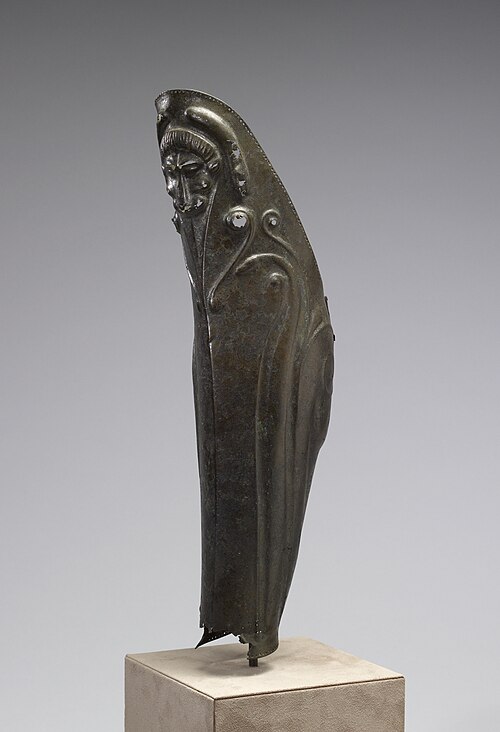 Jambe gauche d'un hoplite grec. Cet exemplaire présente une décoration élaborée en repoussé (une technique dans laquelle le métal est imprimé par l'arrière pour former un motif en relief), notamment une tête de lion sur le genou et des lignes soulignant les muscles du mollet. De minuscules trous bordant les bords supérieur et inférieur fixaient une doublure en tissu et des lanières de cuir.