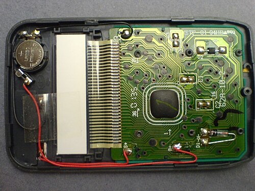 L'intérieur d'une calculatrice de poche récente (vers 2000). Elle utilise une pile bouton associée à une cellule solaire. Le processeur est de type "Chip on Board", recouvert d'époxy foncé.