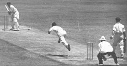 Un joueur de cricket vient de lancer une balle vers un batteur, qui attend l'arrivée de la balle.