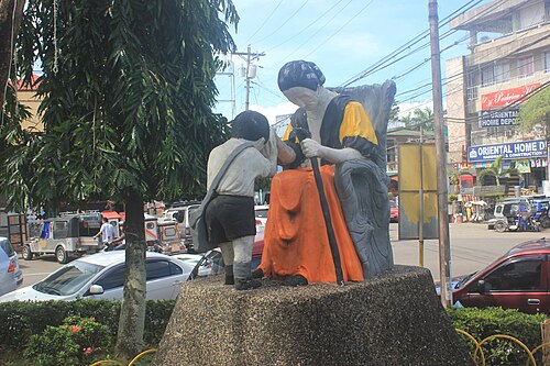 Statue extérieure colorée d'un enfant appuyant son front sur la main d'un aîné assis
