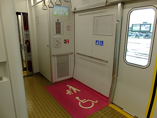 Espace pour fauteuil roulant à l'extrémité d'un train japonais avec le sol peint en rose pour améliorer la visibilité