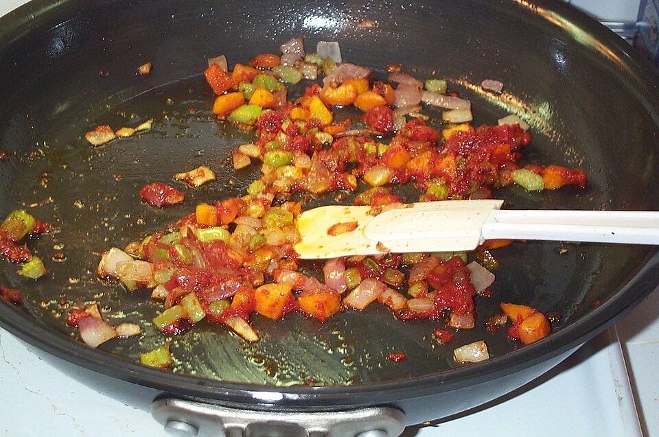 Oignons brunâtres avec carottes et céleri dans une poêle.