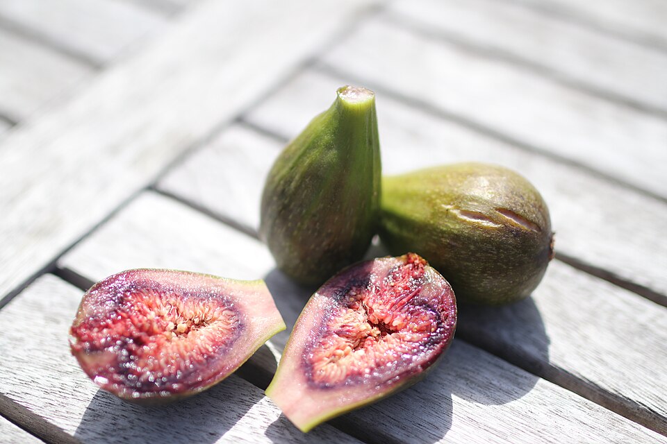 Deux figues entières et deux demi-figues coupées en tranches sur une table en bois, à la lumière naturelle.