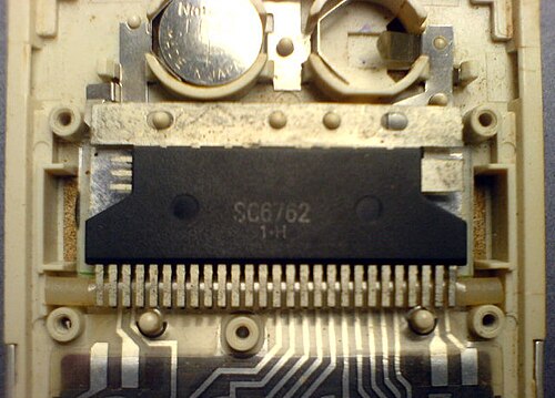 Le processeur (circuit intégré) à l'intérieur d'une calculatrice de poche Sharp des années 1980, marqué SC6762 1•H. Un écran LCD se trouve directement sous la puce. Il s'agissait d'une conception sans PCB. Aucun composant discret n'est utilisé. Le compartiment à piles en haut peut contenir deux piles bouton.