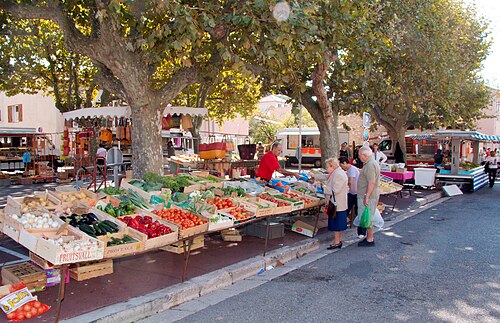 Scène extérieure montrant des étals de marché remplis de fruits et légumes aux couleurs vives
