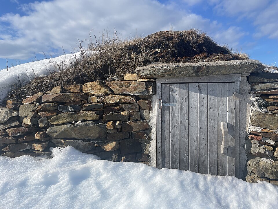 Une porte en bois, encastrée dans un cadre en pierre, partiellement recouverte de neige