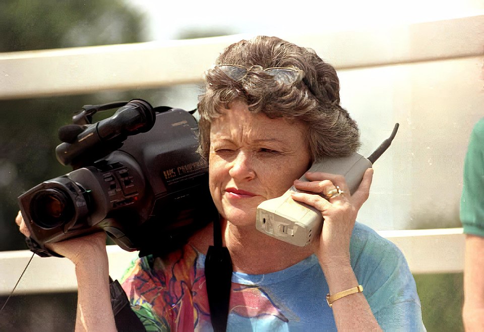 La journaliste Lucy Morgan tenant l'un des premiers téléphones portables en brique, ainsi qu'une caméra vidéo des années 1980