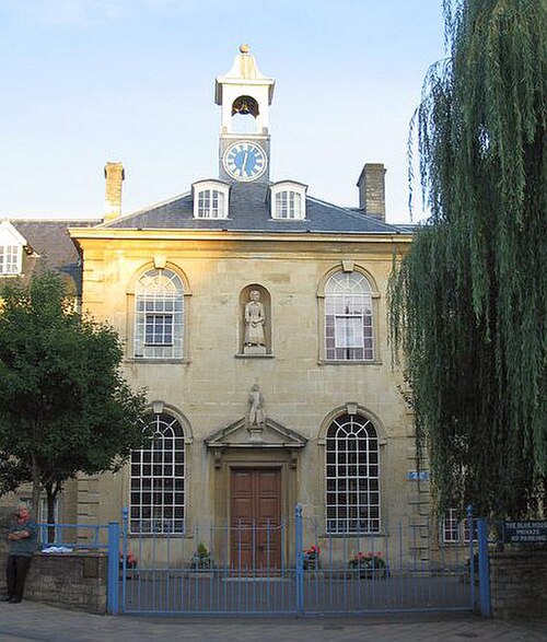 Bâtiment en pierre jaune avec bloc central de 2 étages avec fenêtres cintrées, toit en croupe et tour de l'horloge