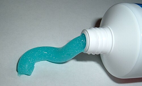 Une photo de l'extrémité d'un tube de dentifrice qui a une ouverture fabriquée avec du dentifrice bleu qui s'étend vers l'extérieur