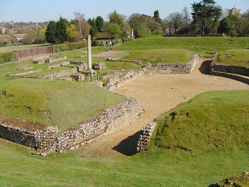 Théâtre romain, entrée en terre battue et scène centrale entourées de buttes de sièges couvertes d'herbe (ruines)