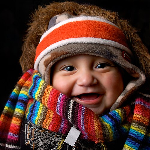 Un bébé portant de nombreux vêtements d'hiver doux : bandeau, bonnet, manteau doublé de fourrure, écharpe et pull, exprimant le confort des vêtements