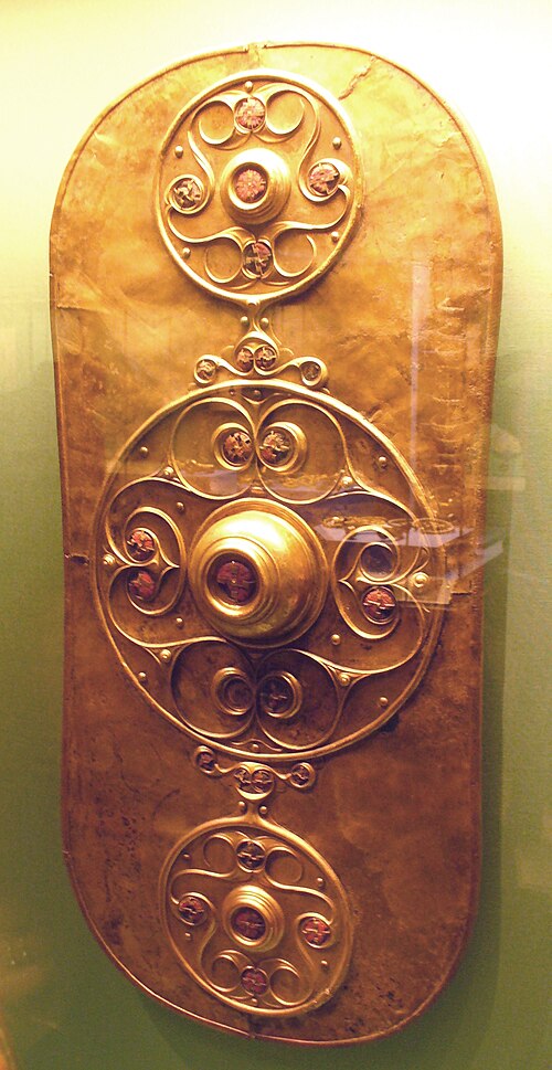 Écu d'or orné de trois motifs circulaires. Le motif central, plus grand, présente un umbo entouré de volutes. Les motifs situés au-dessus et en dessous sont similaires.