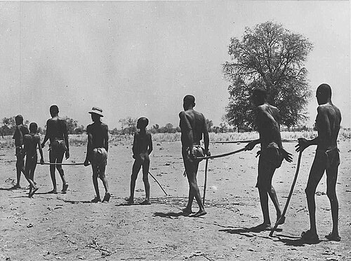 Photographie en noir et blanc d'enfants menant une file d'adultes à travers un paysage sec
