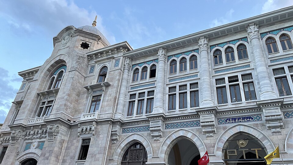 An arched neoclassical building with hanging PTT banners