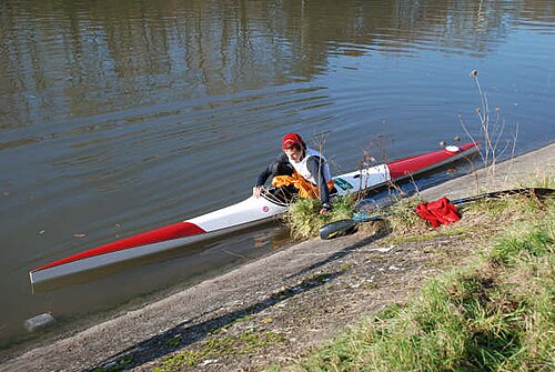 Kayak long et fin avec proue et poupe émoussées, sur eau plate, personne montant à bord