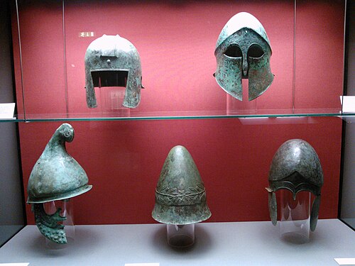 Casques grecs antiques. Ligne supérieure, de gauche à droite : casque de type illyrien, casque corinthien. Ligne inférieure, de gauche à droite : casque de type phrygien, casque Pileus avec ornement en forme de branche d'olivier, casque chalcidien. Staatliche Antikensammlungen