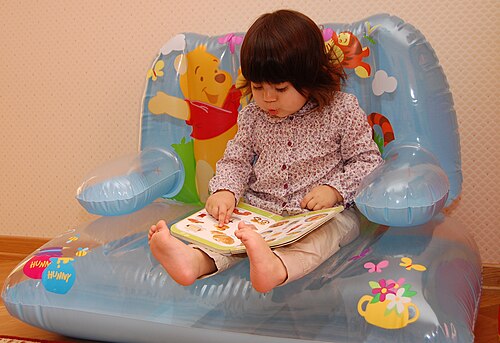 Une fille est assise et regarde un livre d'images qui repose sur ses jambes, tandis qu'elle pose son doigt sur une image.