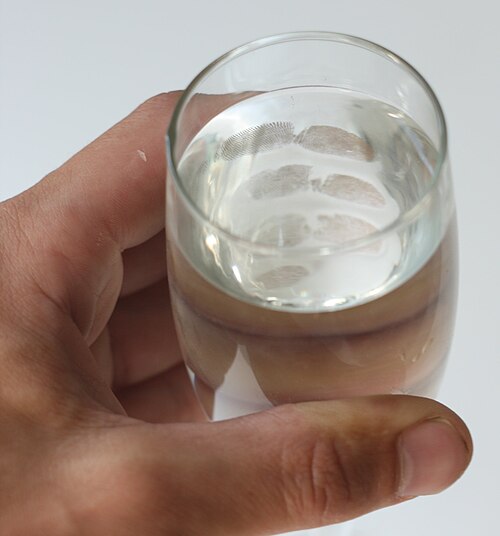 Une main tenant un verre d'eau avec des empreintes digitales visibles de l'intérieur.