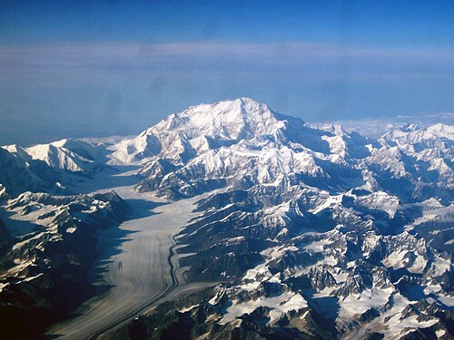 Sur une image aérienne, une montagne est entourée de nombreuses montagnes plus petites et d'un glacier
