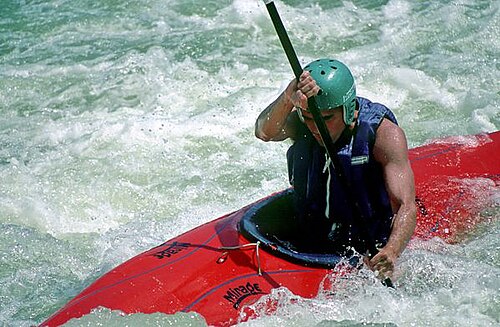 Un homme portant un casque assis dans un bateau en fibre de verre, pagayant dans l'eau mousseuse