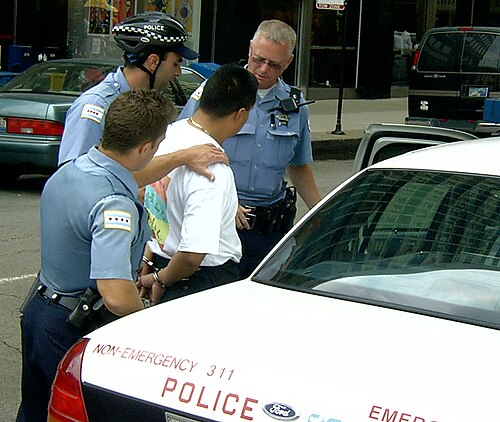 trois policiers encerclent un homme en tee-shirt qui est menotté