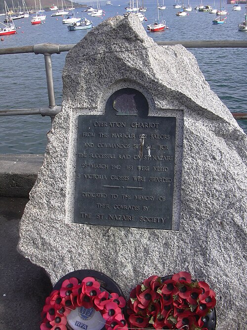 Rocher blanc avec plaque métallique à l'avant ; yachts au mouillage en arrière-plan