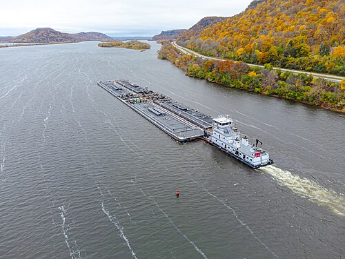 Un petit bateau pousse une grande barge plate sur une large rivière à l'automne