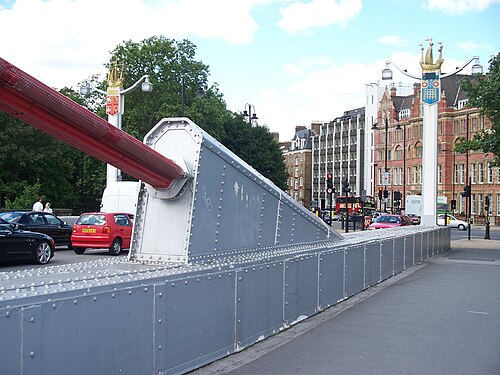 Extrémité d'un gros câble de suspension rouge, fixé à une saillie sur le côté du tablier du pont.