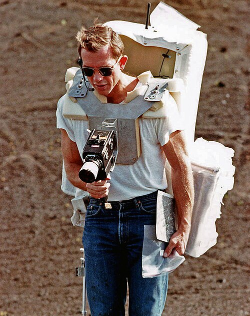 Un homme d'environ 40 ans portant des lunettes de soleil et un grand sac à dos prend une photo avec un appareil photo monté sur sa poitrine