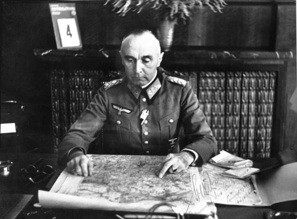 une photographie en noir et blanc d'un homme assis en uniforme regardant une carte